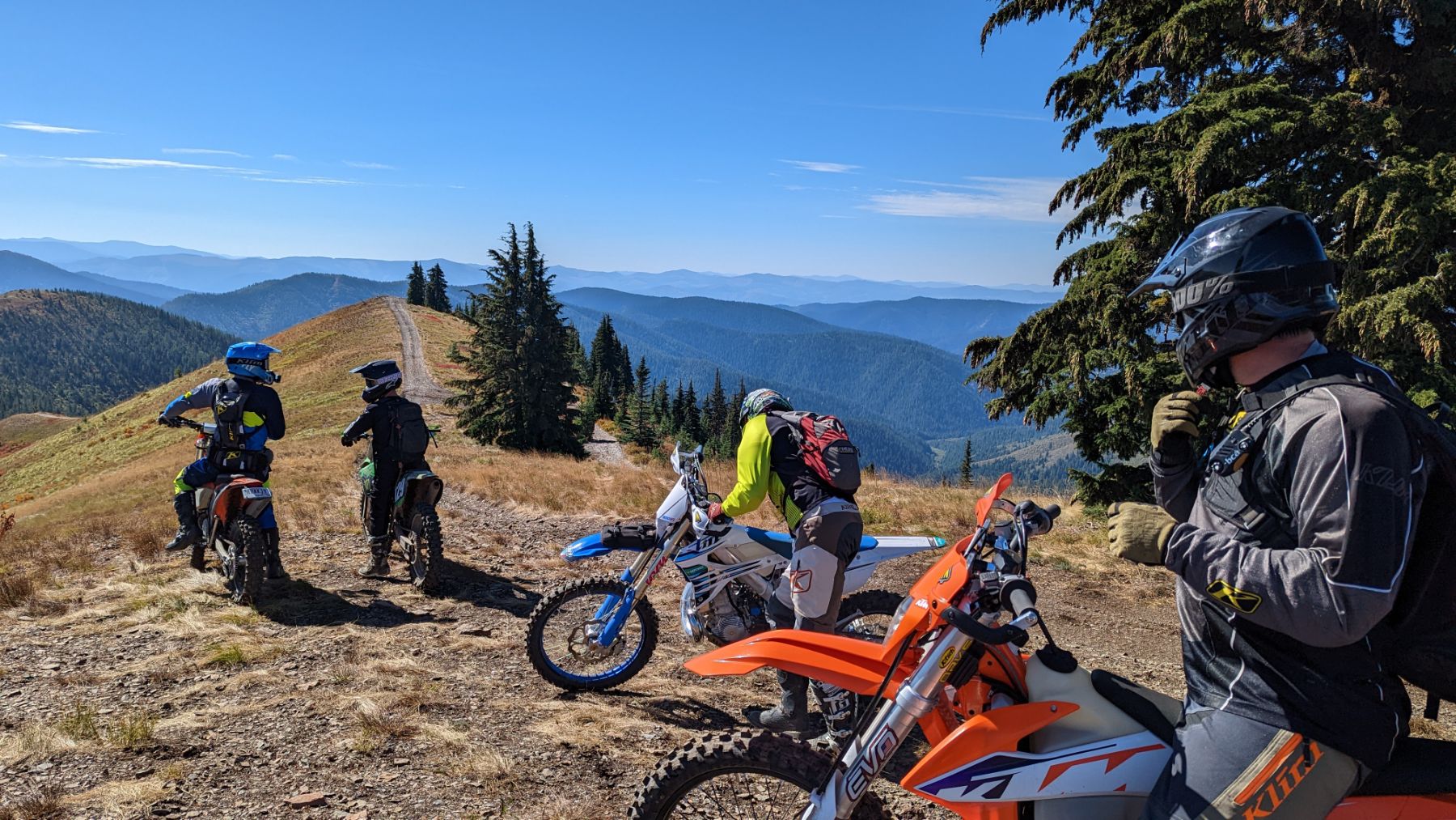 Dirt bike riders pausing on a high North Idaho ridge with layered mountain views