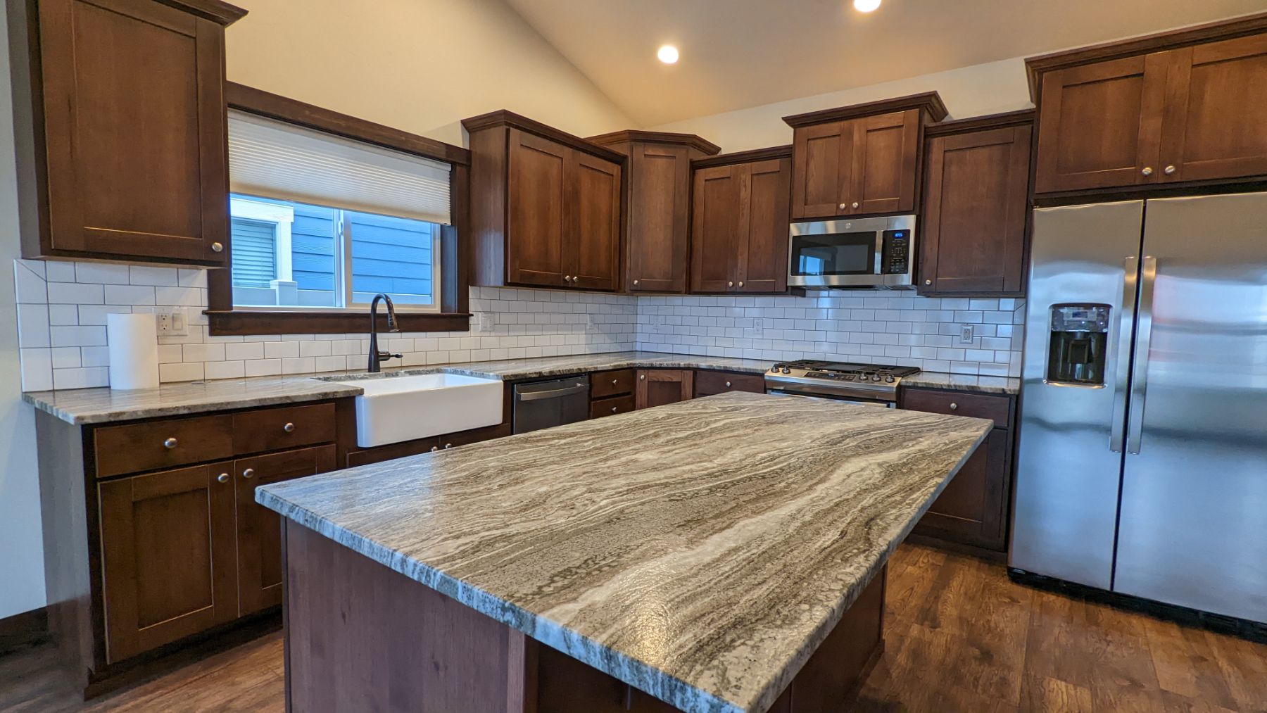 New construction kitchen with quartz island, subtle cabinetry, and stainless appliances
